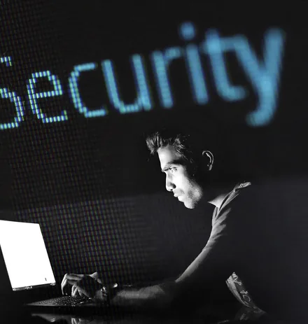A man working at a computer in front of a large screen reading Security